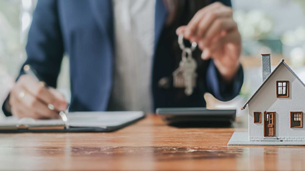 This image shows a mortgage broker in Bend, Oregon, holding a house key and writing on a contract, symbolizing the finalization of a conventional mortgage agreement.